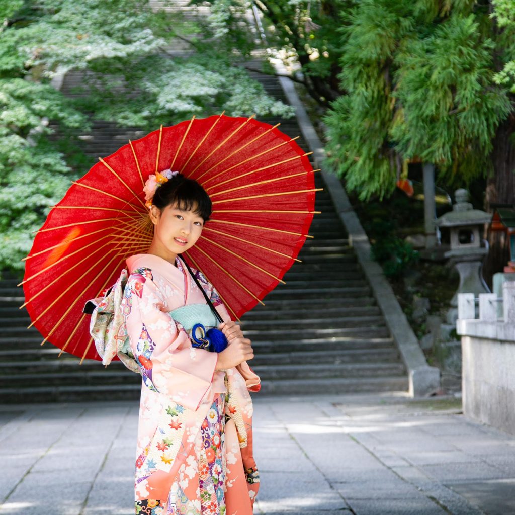 赤い和傘を持って神社で十三詣りのロケーション撮影をする女の子