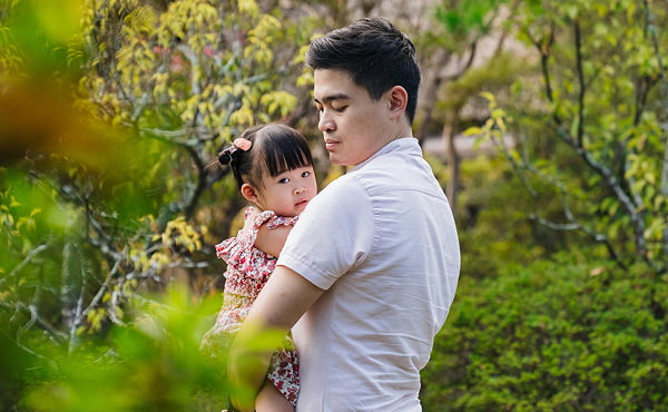 A loving father holding his daughter during a family trip to Japan, captured in a scenic Kyoto park.