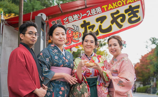 A fun candid photo of travelers in front of a Takoyaki stand in Osaka, capturing the vibrant street food culture of Japan.