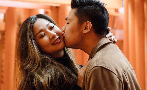 A romantic couple sharing a kiss under the red Torii gates of Fushimi Inari Shrine during their Japan photography tour.